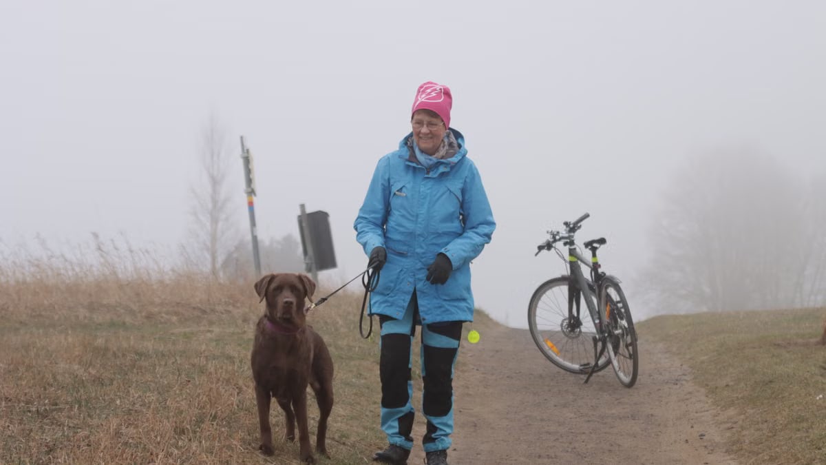 Woman walking Labrador Retriever on a foggy day in Jönköping, Sweden with a bicycle nearby.